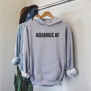 Op de afbeelding: Grijs hoodie met de tekst "AQUARIUS AF" in het zwart op de voorkant.