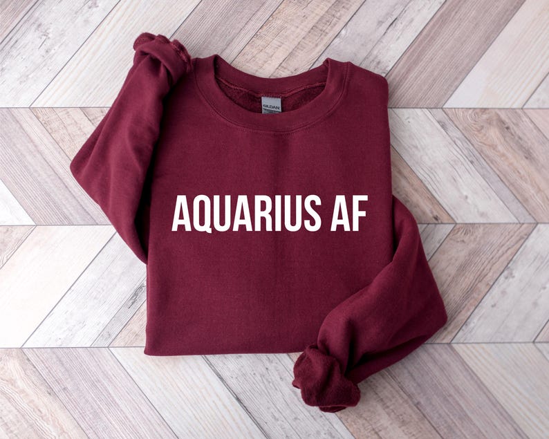 Op de afbeelding: Een bordeauxrood sweatshirt met de tekst "Aquarius AF" in wit gedrukt op de voorkant.