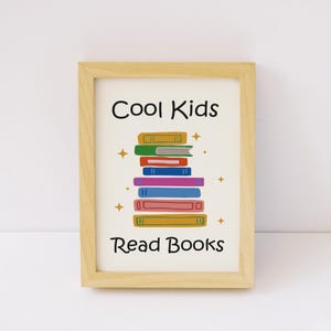 Peut inclure: Un cadre en bois clair contenant une impression blanche avec le texte noir Cool Kids Read Books. Au centre, une pile de livres illustrés colorés dans des tons jaune, rouge, bleu, violet et vert, agrémentée de petites étoiles dorées.