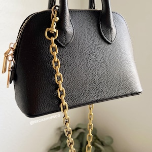 May include: A black leather handbag with a gold chain strap. The bag has a top handle and a zip closure.