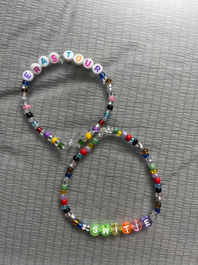 May include: Two colorful beaded necklaces with letter beads spelling out "ERA TOUR" and "SWITIE".