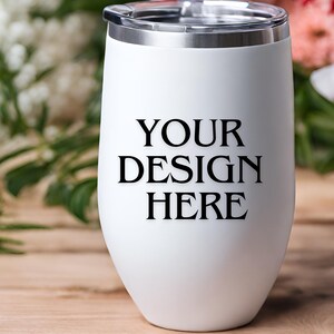 Peut inclure: Un gobelet &agrave; vin en acier inoxydable blanc avec un couvercle argent&eacute;. Le gobelet porte l'inscription "YOUR DESIGN HERE" imprim&eacute;e sur le devant.