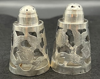 May include: A pair of silver salt and pepper shakers with a clear glass base and intricate floral designs.