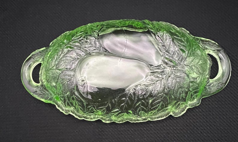May include: A green glass serving dish with a pear design. The dish has a leaf pattern around the pears and handles on each side. The dish is approximately 10 inches long and 6 inches wide.