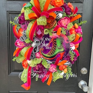 May include: A colorful wreath with a variety of flowers, ribbons, and a decorative sign. The sign features a green boot with the text "If the shoe fits." The wreath includes orange, pink, green, and purple elements.