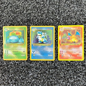May include: Three Pokemon trading cards featuring Venusaur, Blastoise, and Charizard. The cards are in excellent condition and have a holographic finish.