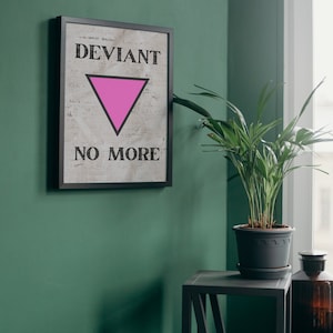 Peut inclure: Une impression encadrée avec un triangle rose et le texte "Deviant No More" sur un mur vert. Une plante en pot est posée sur une table d'appoint noire.