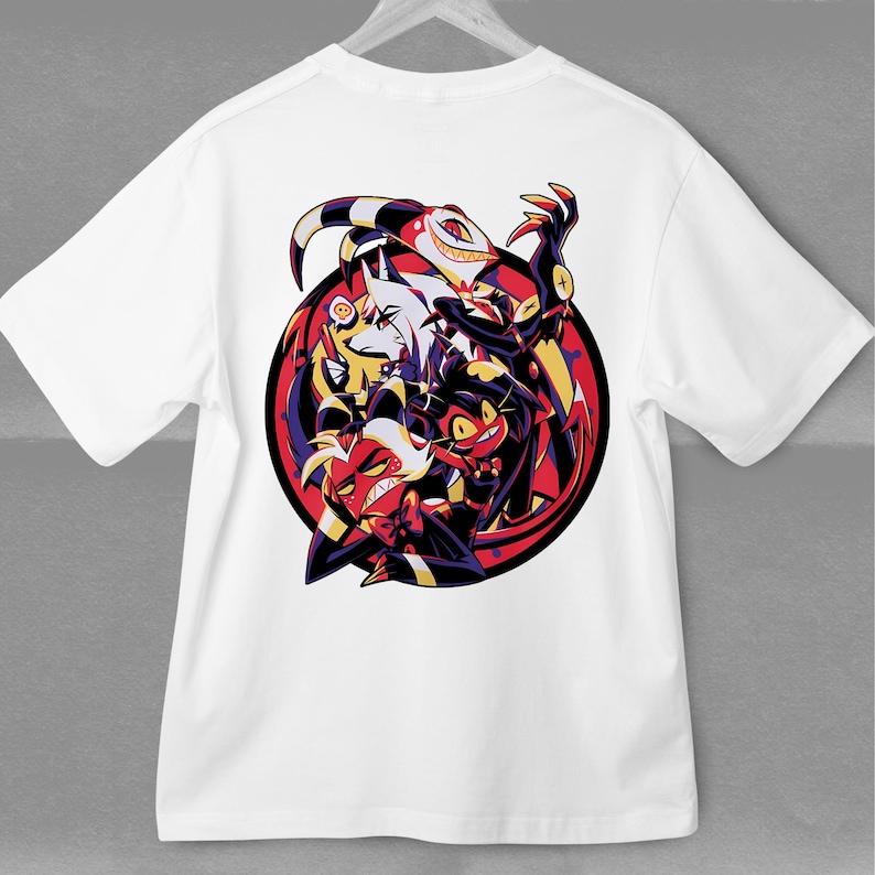 May include: White t-shirt featuring a colorful graphic of cartoon characters within a red and black circular design. The artwork includes characters with horns, sharp teeth, and various expressions. The shirt is hanging on a white hanger.