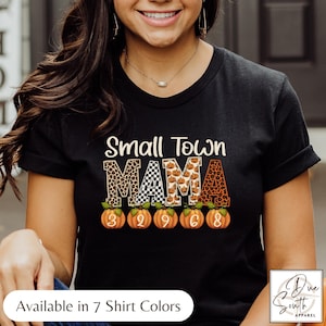 May include: Black t-shirt with the text "Small Town MAMA" in a mix of fonts and patterns, including leopard print and pumpkins. The numbers 3, 2, 9, 6, and 8 are printed on pumpkins below the text. The shirt is from Due South Apparel.