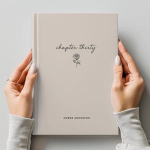 May include: A beige journal held by two hands. The cover features the words "chapter thirty" in a script font, along with a small rose illustration. The name "AMBER ANDERSON" is printed at the bottom of the cover.