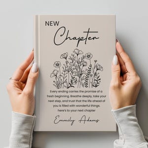May include: A book cover with the words "NEW Chapter" in black script. Below the title is a floral illustration. The cover also includes the text "Every ending carries the promise of a fresh beginning...here's to your next chapter" and the name "Emmily Adams."