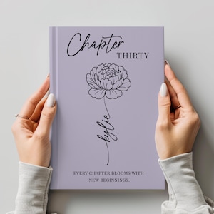 May include: A lavender journal with the words "Chapter Thirty" and "kylie" in black script. A floral illustration is centered on the cover. The phrase "EVERY CHAPTER BLOOMS WITH NEW BEGINNINGS" is printed at the bottom.