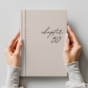 May include: A light beige hardcover book with a vertical black line and the text CLAIRE MITCHELL printed on the left side. The front cover features the black script text chapter and the number 50 written in a large, bold, black font.