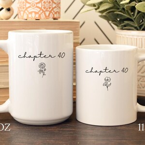 May include: Two white ceramic mugs with black text reading chapter 40 and a small floral line drawing. The larger mug is labeled 15 oz and the smaller mug is labeled 11 oz. Both mugs feature a side handle and a smooth, cylindrical body design.