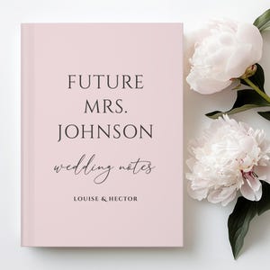 May include: A light pink wedding notebook with the text "FUTURE MRS. JOHNSON wedding notes" in black. The names "LOUISE & HECTOR" are printed at the bottom. White peonies are in the background.