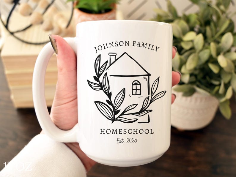 May include: White ceramic mug with a black line drawing of a house, leaves, and text that reads "JOHNSON FAMILY HOMESCHOOL Est. 2025". The mug is held by a person.
