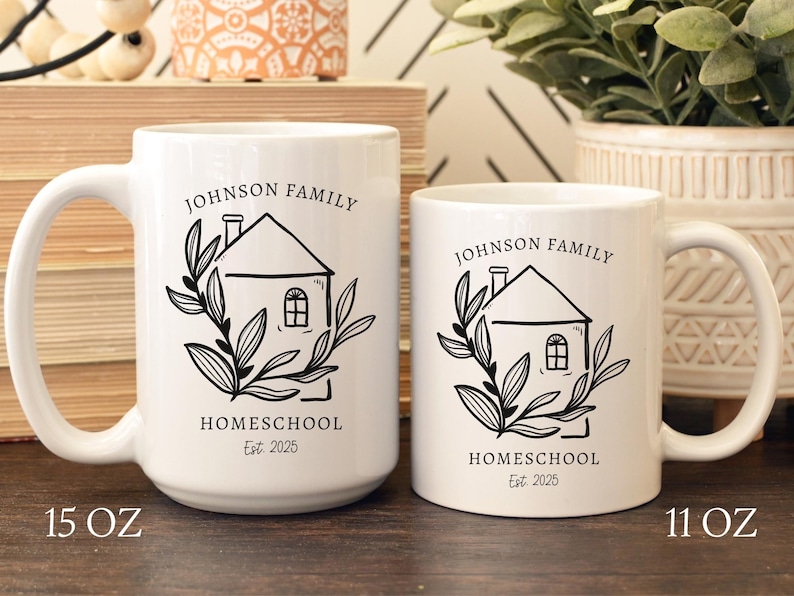 May include: Two white ceramic mugs with black text and graphics. The mugs have a house design with the words "JOHNSON FAMILY HOMESCHOOL Est. 2025". The larger mug is 15 oz, and the smaller mug is 11 oz.