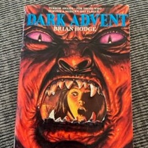 May include: A paperback book cover with a red, demonic face with a large open mouth. A woman's face is visible in the mouth, looking scared. The book title is "Dark Advent" by Brian Hodge.