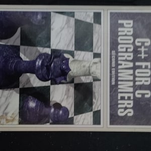 May include: A book titled "C++ for C Programmers" by Ira Pohl, second edition. The cover features a 3D chessboard with a purple chess piece and a white chess piece.