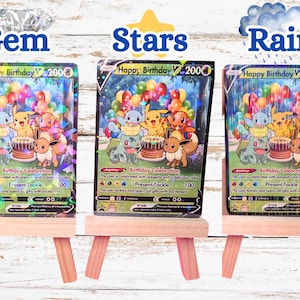 May include: Three Happy Birthday V trading cards displayed on small wooden easels. Each card features Pikachu, Squirtle, Charmander, Bulbasaur, and Eevee with a birthday cake and balloons. The cards have distinct holographic patterns: Gem, Stars, and Rain.