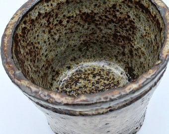 May include: A small, brown and white ceramic bowl with a rough, textured surface. The bowl is empty and has a slightly rounded shape.