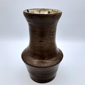 Può includere: Un vaso in ceramica marrone con un bordo bianco. Il vaso ha una superficie testurizzata e un'apertura leggermente svasata.