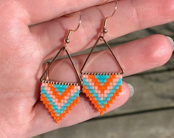 May include: A pair of gold triangle earrings with a geometric pattern of orange, pink, and turquoise beads.