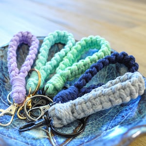 May include: A set of four colourful crocheted keyrings with gold and silver key rings. The keyrings are made of different shades of blue, green, and purple.