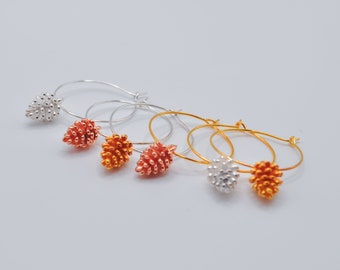 May include: Three pairs of hoop earrings with a pine cone design. The earrings are silver, gold, and rose gold.