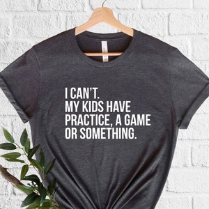 May include: A dark gray t-shirt with white text that reads "I can't. My kids have practice, a game or something."