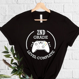 May include: Black t-shirt with a white graphic of a video game controller and the text "2nd Grade Level Complete".