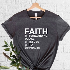 以下が含まれることがあります： 白い文字で「FAITH」とプリントされた濃いグレーのTシャツ。文字は「Forwarding All Issues To Heaven」の頭文字です。