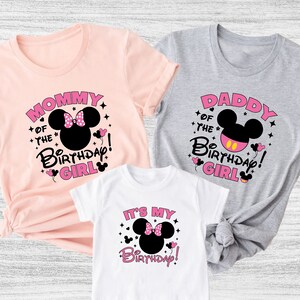 Puede incluir: Tres camisetas con dise&ntilde;os de cumplea&ntilde;os. Las camisetas son rosas, grises y blancas. Cada camiseta presenta un gr&aacute;fico de la cabeza de Minnie Mouse y las frases "Mommy of the Birthday Girl", "Daddy of the Birthday Girl" y "It's My Birthday!"