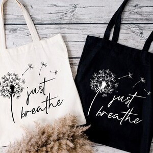 May include: Two tote bags with the text "just breathe" and a dandelion graphic. One bag is white with black text and graphic, the other is black with white text and graphic.