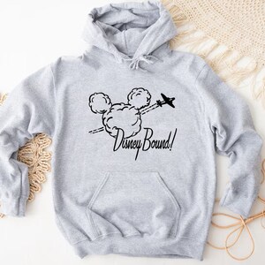Puede incluir: Sudadera gris con capucha con un gr&aacute;fico negro de la cabeza de Mickey Mouse y el texto "Disney Bound!" impreso en la parte delantera.