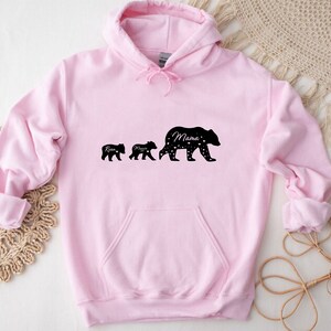 May include: Pink hooded sweatshirt with a black silhouette of three bears. The largest bear says "Mama" and the two smaller bears say "Ryan" and "Mason".