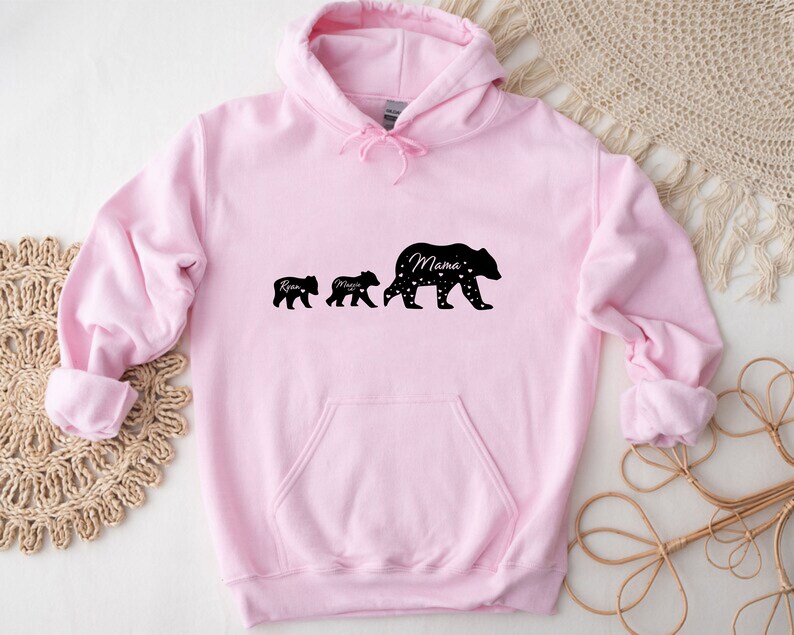 May include: Pink hooded sweatshirt with a black silhouette of three bears. The largest bear says "Mama" and the two smaller bears say "Ryan" and "Mason".