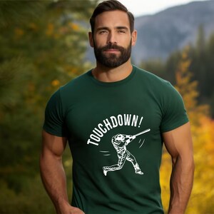 May include: A green t-shirt with a white graphic of a baseball player swinging a bat and the text "TOUCHDOWN!"