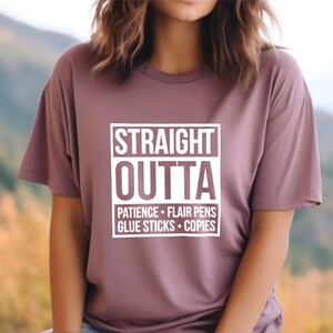 May include: A mauve-colored t-shirt with the words "STRAIGHT OUTTA" in a white, bold font, with the words "PATIENCE &bull; FLAIR PENS &bull; GLUE STICKS &bull; COPIES" below. The shirt has short sleeves.