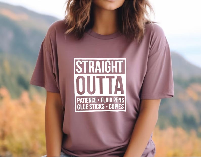 May include: A mauve-colored t-shirt with the words "STRAIGHT OUTTA" in a white, bold font, with the words "PATIENCE &bull; FLAIR PENS &bull; GLUE STICKS &bull; COPIES" below. The shirt has short sleeves.