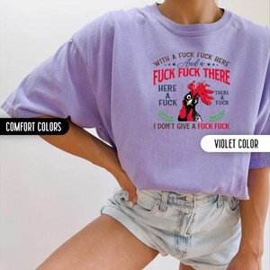 May include: A violet-colored t-shirt with the text "WITH A FUCK FUCK HERE And a FUCK FUCK THERE HERE A FUCK THERE A FUCK I DON'T GIVE A FUCK FUCK" and a rooster graphic. The shirt is labeled "COMFORT COLORS" and "VIOLET COLOR".