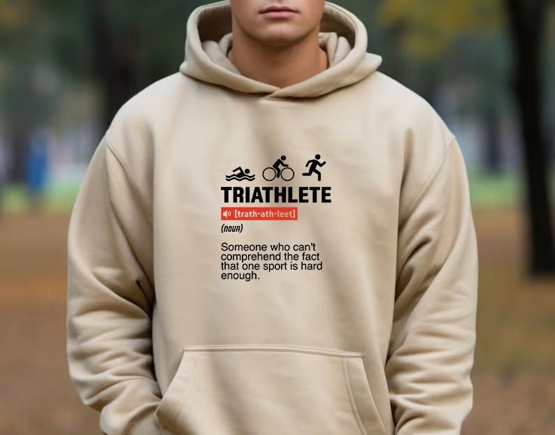 以下が含まれることがあります： トライアスロンの言葉が「トライアスロン」と定義され、「1つのスポーツが十分に難しいという事実を理解できない人」と定義された、ベージュのフード付きスウェットシャツ。グラフィックには、スイマー、サイクリスト、ランナーのアイコンも含まれています。