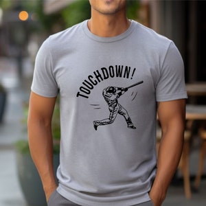 May include: A gray t-shirt with a black graphic of a baseball player swinging a bat. The text "TOUCHDOWN!" is printed above the player.