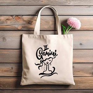 May include: A white canvas tote bag with black text and a graphic of a woman's face. The text reads "II Gemini".