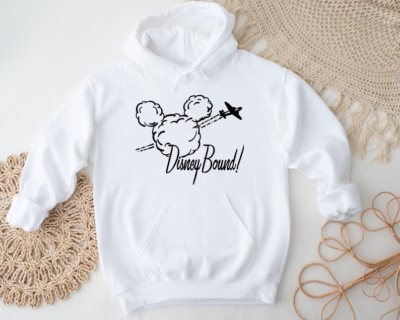 Puede incluir: Sudadera con capucha blanca con un gr&aacute;fico negro de las orejas de Mickey Mouse con un avi&oacute;n volando a trav&eacute;s de ellas y el texto "Disney Bound!"