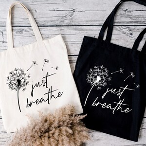 May include: Two tote bags with the text "just breathe" and a dandelion graphic. One bag is white with black text and graphic, the other is black with white text and graphic.