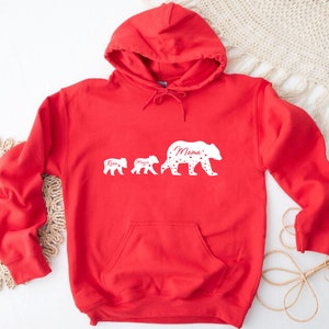 May include: Red hooded sweatshirt with a white silhouette of three bears. The largest bear says "Mama" and the smaller bears say "Ryan" and "Maya".