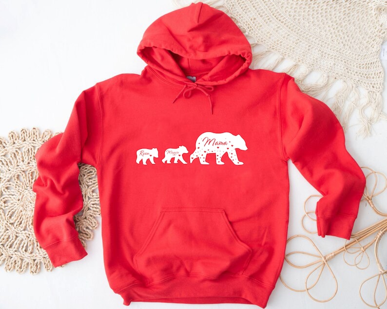 May include: Red hooded sweatshirt with a white silhouette of three bears. The largest bear says "Mama" and the smaller bears say "Ryan" and "Maya".