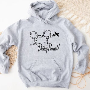 Puede incluir: Sudadera gris con capucha con un gr&aacute;fico negro de la cabeza de Mickey Mouse y el texto "Disney Bound!" impreso en la parte delantera.