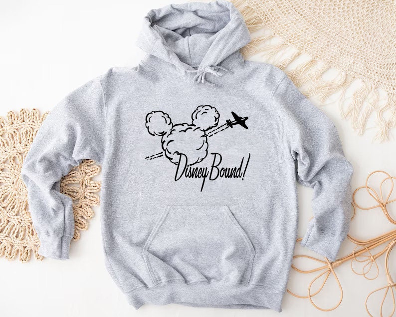 Puede incluir: Sudadera gris con capucha con un gr&aacute;fico negro de la cabeza de Mickey Mouse y el texto "Disney Bound!" impreso en la parte delantera.